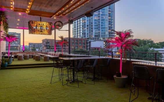 Terraza exterior con césped artificial, palmeras y vista a la ciudad al atardecer