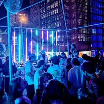 Escena nocturna en la terraza con luces de neón y gente socializando