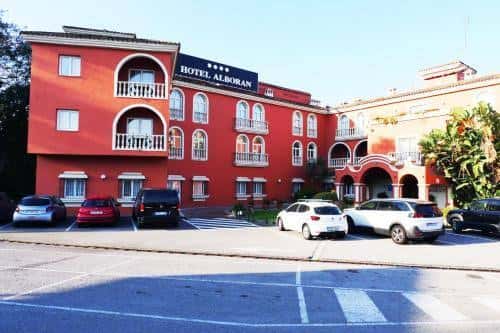Vista exterior frontal del Hotel Alborán con su fachada roja y aparcamiento