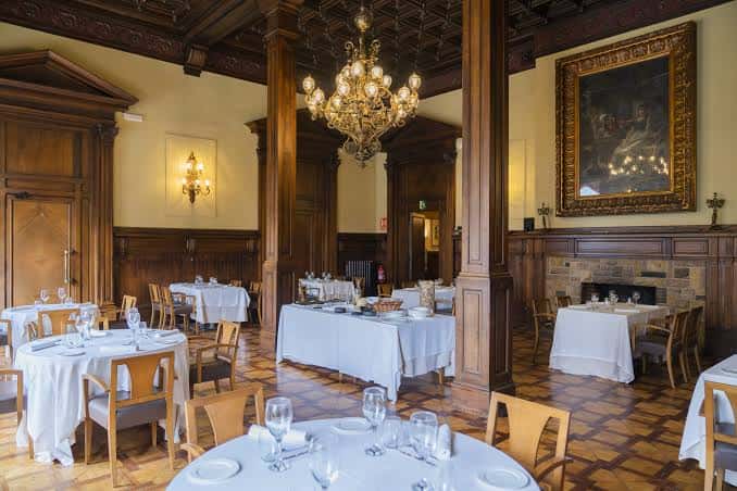 Sala de banquetes con mesas dispuestas para evento, techos ornamentados y chimenea decorativa