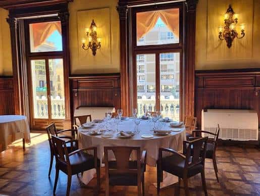 Sala con ventanales y mesa redonda preparada para cena, con vistas al exterior