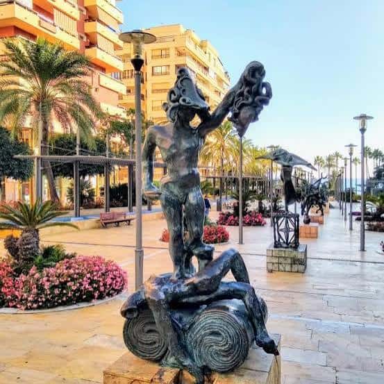 Detalle de escultura artística en la Avenida del Mar con jardines floridos y arquitectura costera