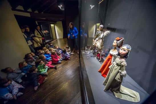 Niños observando títeres de marionetas en una vitrina de la colección