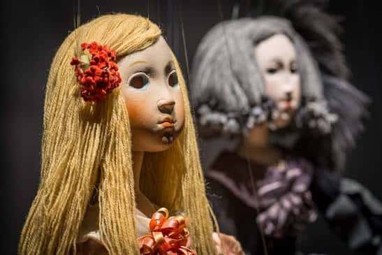 Primer plano de un títere con cabello rubio y flores rojas en la cabeza