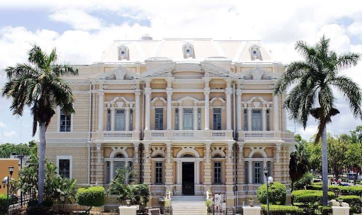 Vista frontal del Palacio Cantón con palmeras y cielo parcialmente nublado