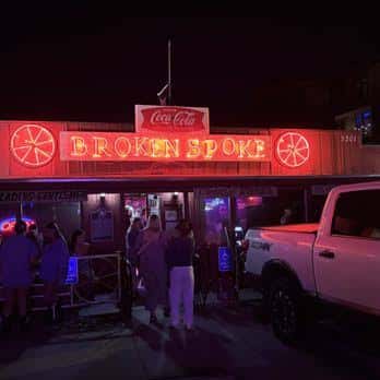 Entrada nocturna del Broken Spoke iluminada con neón, mostrando ambiente festivo y público