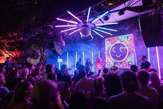 Concierto en vivo en el patio trasero de Cheer Up Charlies con iluminación de neón y público