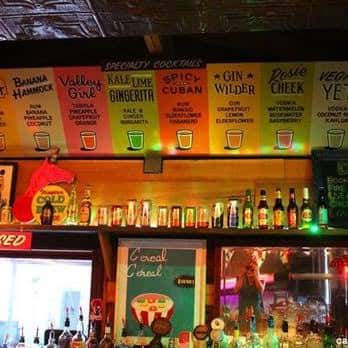 Barra de cócteles con letreros de menú iluminados y botellas de bebidas