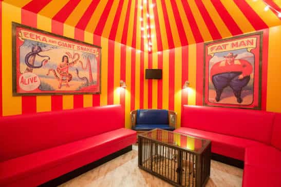 Sala de karaoke con temática de circo, paredes a rayas rojas y amarillas, y sofás rojos