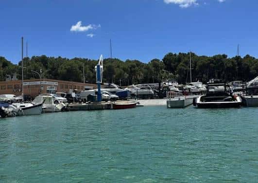 Vista general del puerto deportivo con barcos y el club al fondo bajo un cielo azul