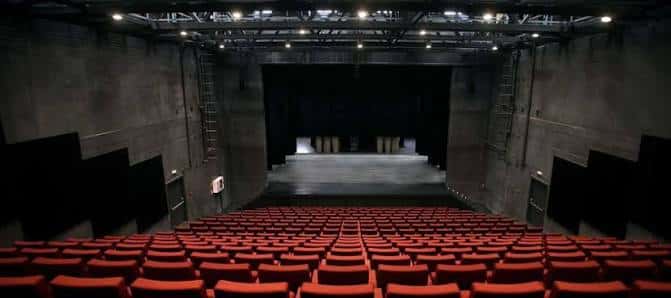 Interior del auditorio con butacas rojas dispuestas en gradas y escenario iluminado