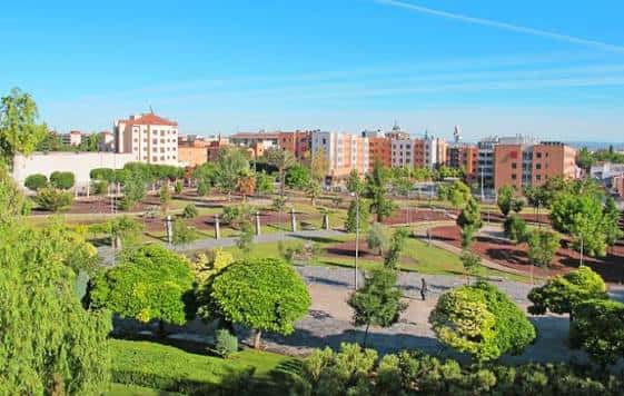 Vista aérea del parque con zonas verdes, senderos y edificios urbanos al fondo