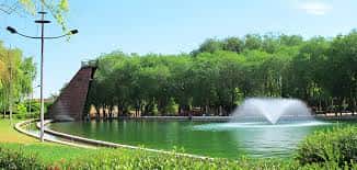 Lago del parque con fuente central y estructura piramidal rodeada de árboles