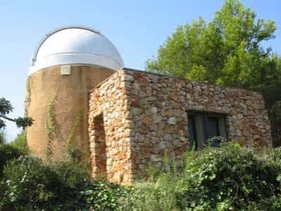 Fachada del observatorio en un día soleado, mostrando la cúpula y la estructura de piedra rodeada de vegetación