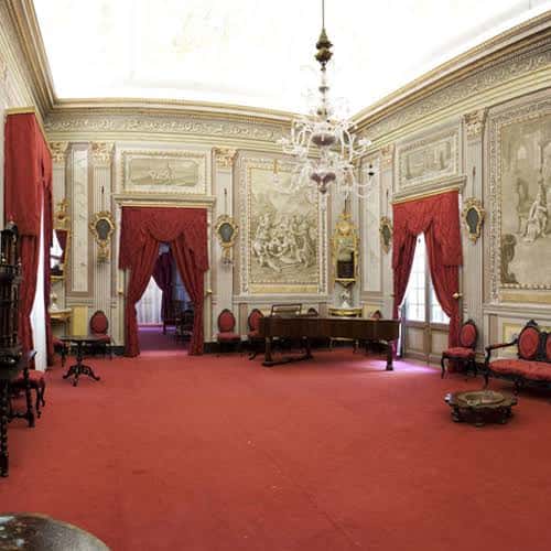 Salón principal con alfombra roja, cortinas y lámpara de araña
