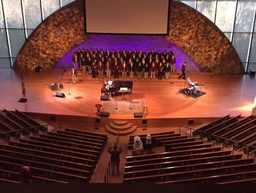 Vista panorámica del auditorio con coro en el escenario y pantalla de proyección