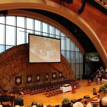 Interior del auditorio con pantalla central y decoración de piedra en el escenario