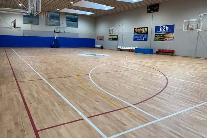 Interior del pabellón con pista de baloncesto de madera y gradas vacías