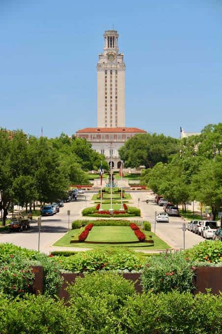 Vista frontal del UT Tower con jardines y banderas en primer plano