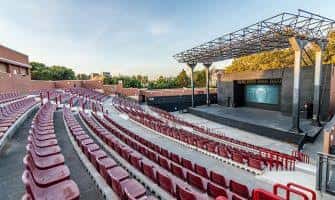Interior del auditorio con gradas de asientos rojos y estructura metálica del escenario