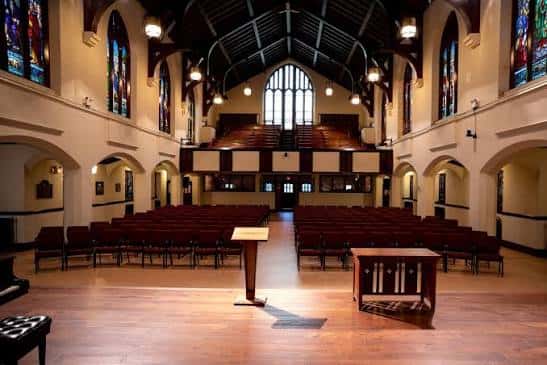 Salón principal de la iglesia con asientos rojos, podio y piano en el escenario