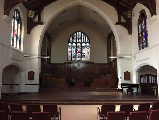 Escenario de la iglesia con banco de madera, órgano y vitrales en el fondo
