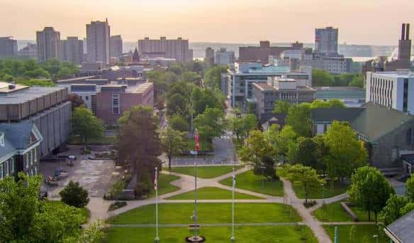 Plaza central del campus con banderas, senderos y vista urbana de Halifax al atardecer