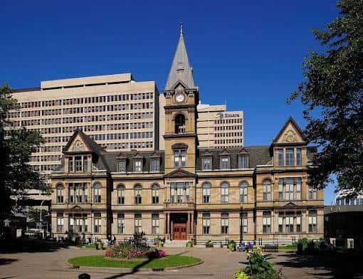 Plaza delantera de Halifax City Hall con jardines y árboles en primer plano, mostrando la fachada principal
