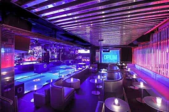 Sala interior del club Opium con iluminación púrpura y mesas redondas