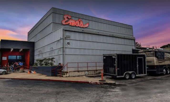 Exterior del edificio de Emo's Austin con el logo rojo en la pared y camiones de tour estacionados