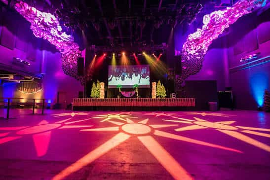 Interior del salón de eventos con escenario, luces de colores y decoración festiva
