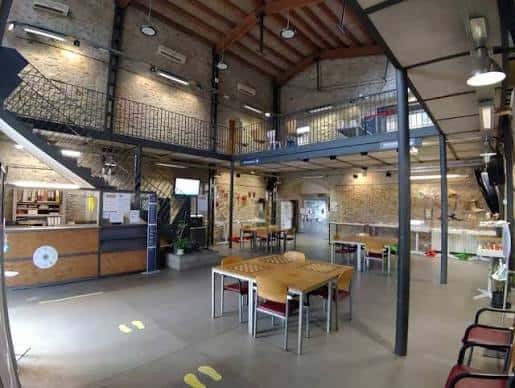 Interior del espacio de eventos con mesas, escalera metálica y estructura de madera, ideal para celebraciones
