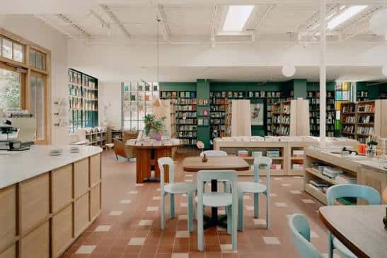 Interior luminoso de la librería con estanterías verdes, mesas de lectura y suelo de baldosas