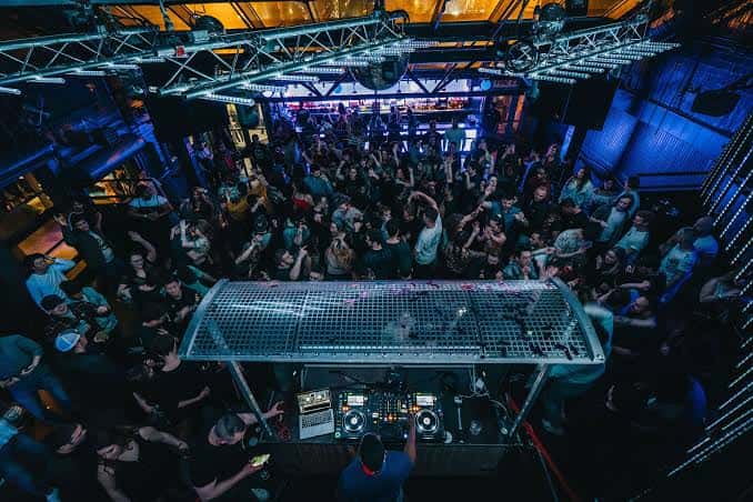 Vista aérea del interior del club con DJ y multitud bailando bajo luces azules
