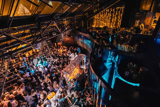 Interior del club con estructura metálica, luces cálidas y público en múltiples niveles