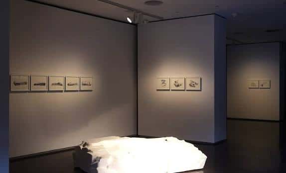 Sala de exposiciones con obras de arte en las paredes y una instalación central iluminada
