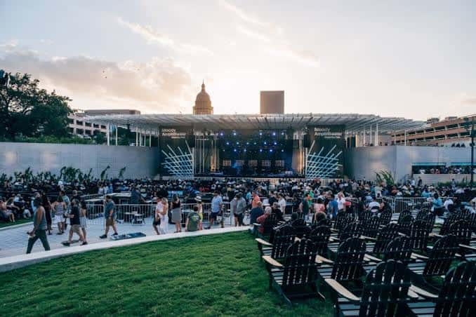 Vista general del Moody Amphitheater durante un concierto al atardecer, con el Capitolio de Texas al fondo