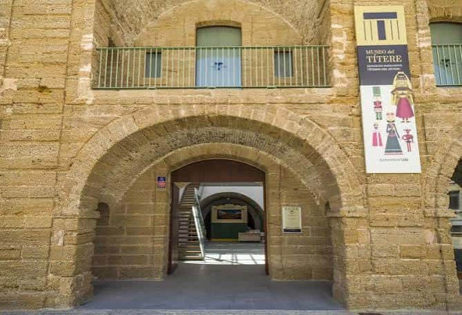 Fachada principal del Museo del Títere en Cádiz con arco de piedra y cartel informativo