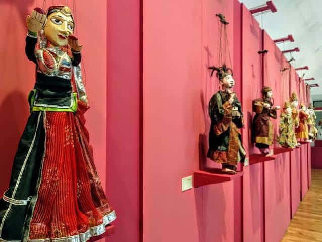 Exposición de marionetas tradicionales en pared rosa con estanterías flotantes