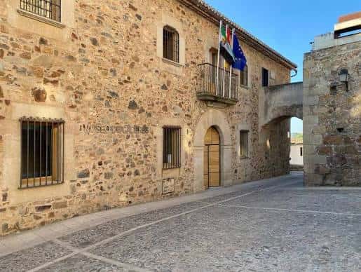 Fachada histórica del Museo de Cáceres con mampostería de piedra y banderas