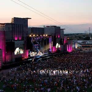 Concierto en vivo en el escenario principal con multitud y luces de colores al atardecer