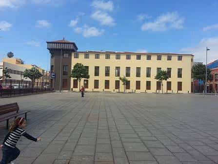 Plaza del Cristo con edificio amarillo y persona caminando en primer plano