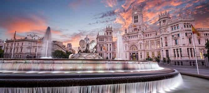 Paisaje panorámico de la Plaza de Cibeles al atardecer con cielos naranjas y la fuente iluminada