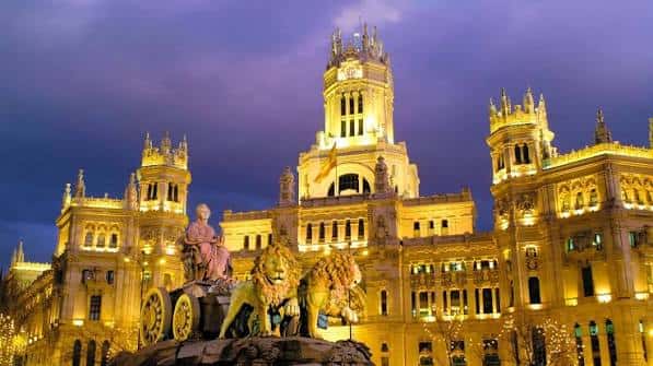 Vista nocturna de la Plaza de Cibeles con el Palacio de Cibeles iluminado en dorado y la fuente en primer plano