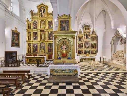 Interior de la iglesia con retablos dorados y suelo de baldosas en damero