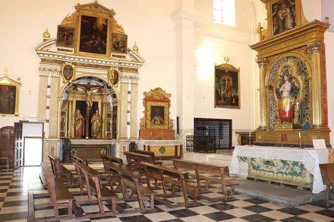 Nave lateral de la iglesia con bancos de madera y altares ornamentados