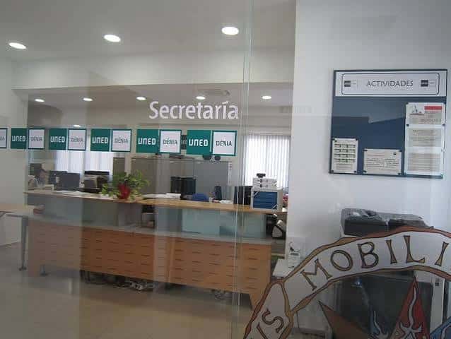 Interior de la secretaría de la UNED Dénia, con mostrador de atención al público y paneles informativos en pared