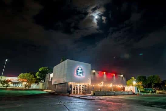 Vista nocturna de la fachada exterior del venue con iluminación y letrero