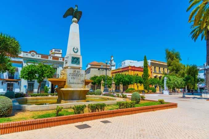 Plaza de las Angustias en día soleado, mostrando el monumento, fuentes y jardines bien cuidados