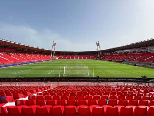 Vista interior del estadio con gradas rojas y campo de fútbol